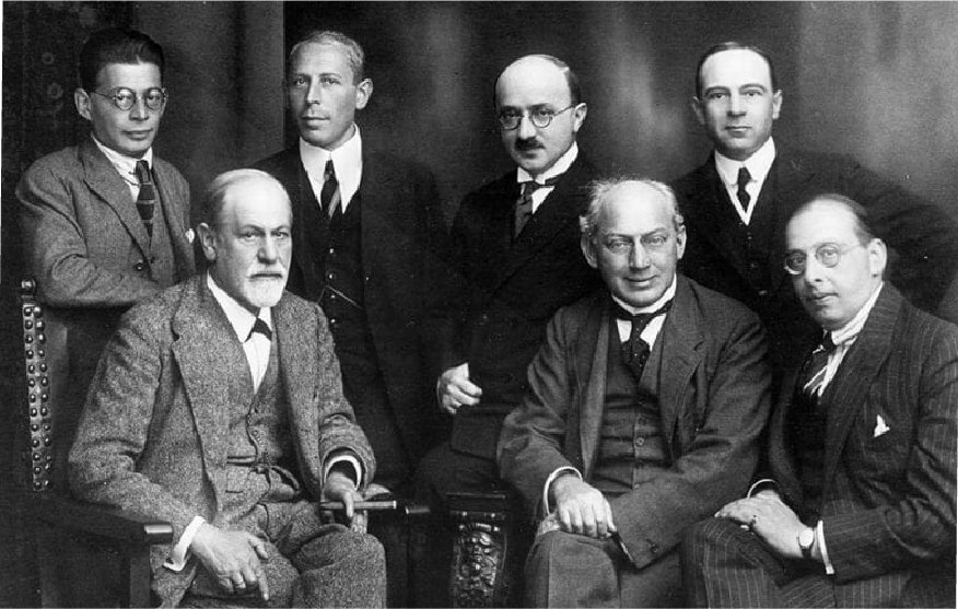 Retrato de grupo, em preto e branco: Freud sentado ao lado de
                  outros dois psicanalistas, com quatro de pé atrás deles.